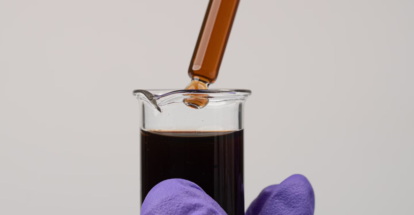 Laboratory dropper adding amber liquid to a dark shilajit sample in a glass beaker