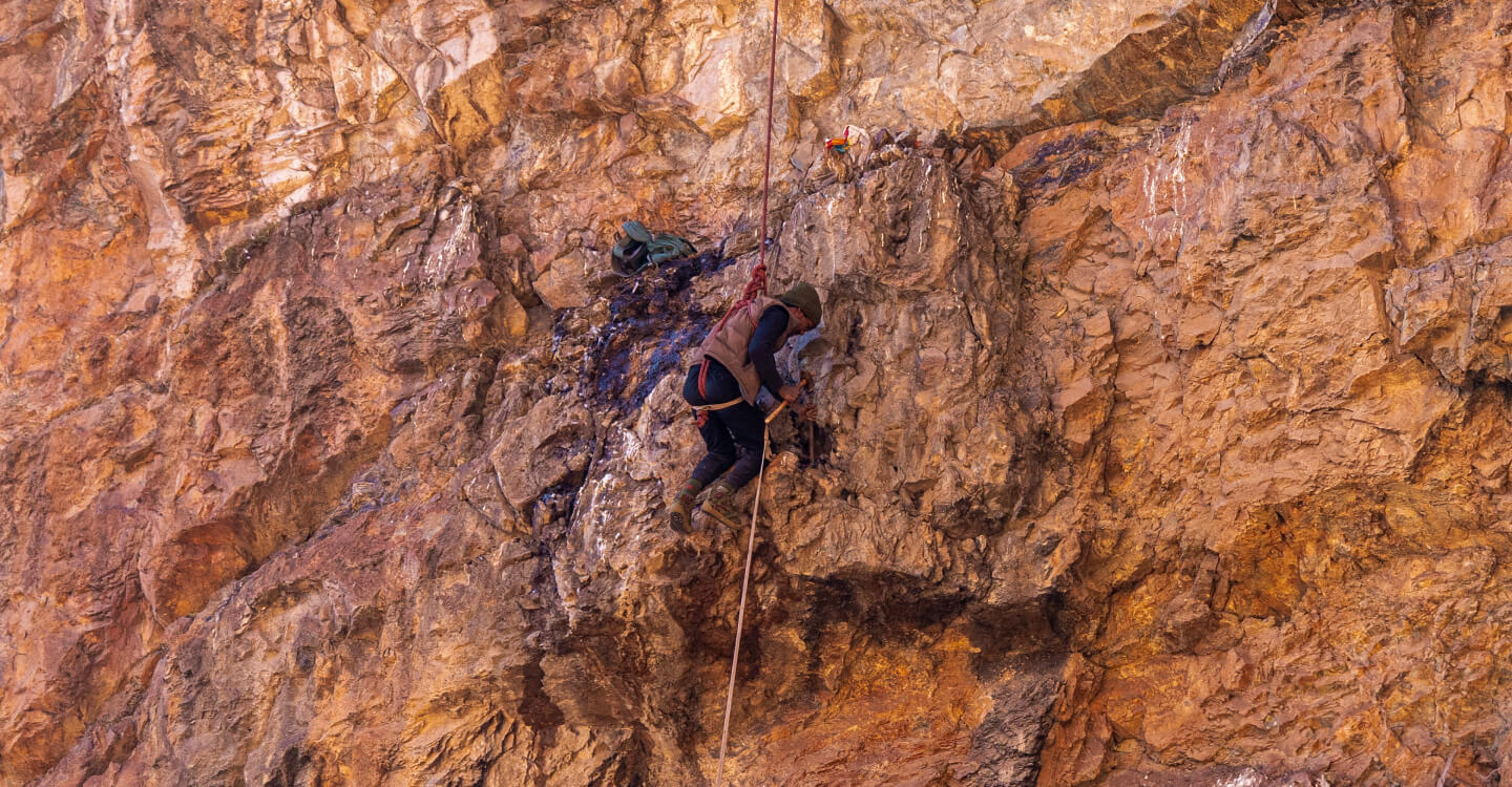A climber harvesting raw shilajit from a rocky mountain cliff, highlighting the natural origin behind the shilajit hype
