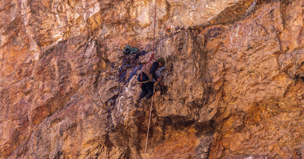 A climber harvesting raw shilajit from a rocky mountain cliff, highlighting the natural origin behind the shilajit hype