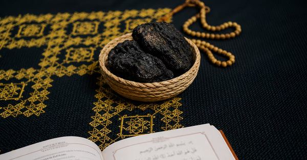 Raw black shilajit in a woven bowl beside prayer beads and an open Quran for a discussion about shilajit and Sunnah