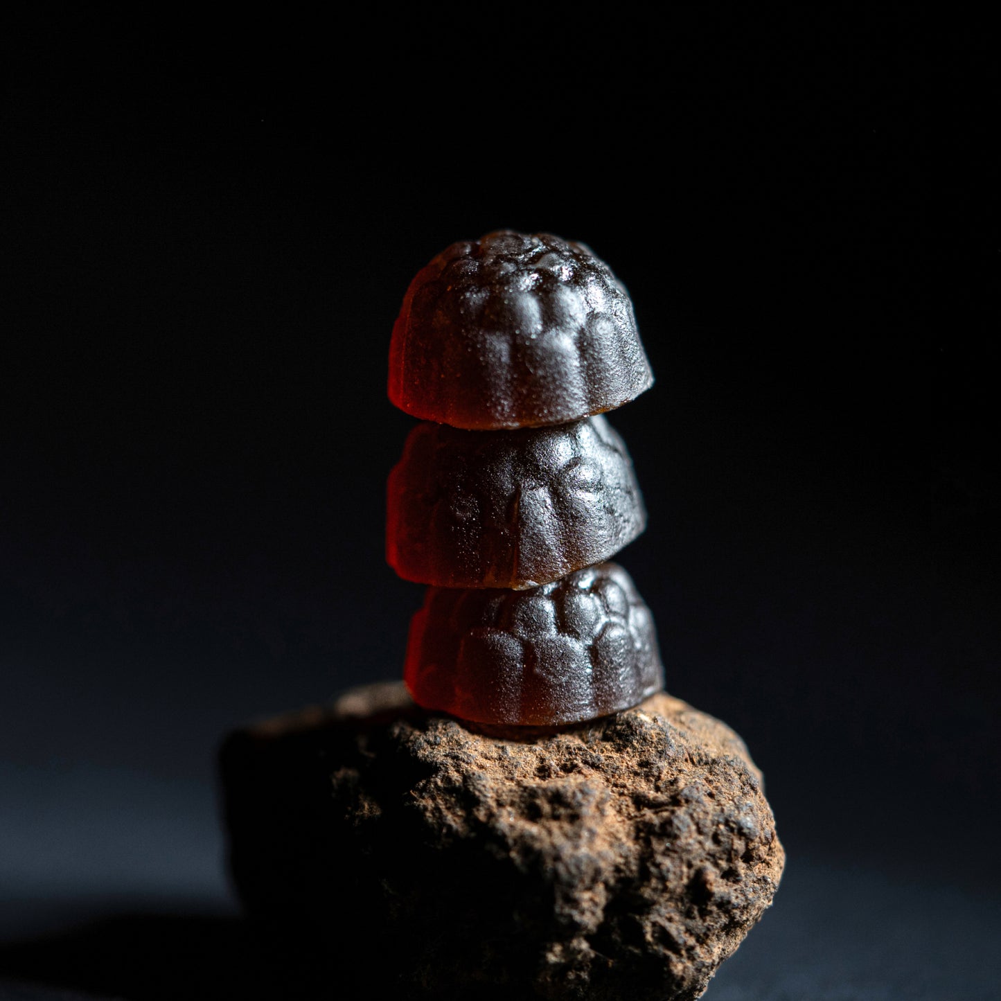 Pure shilajit gummies stacked on natural rock in a dark premium studio setting with rich gummy texture
